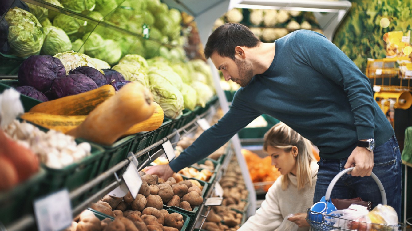 Ein Mann und eine Frau greifen im Supermarkt nach Gemüse im Regal