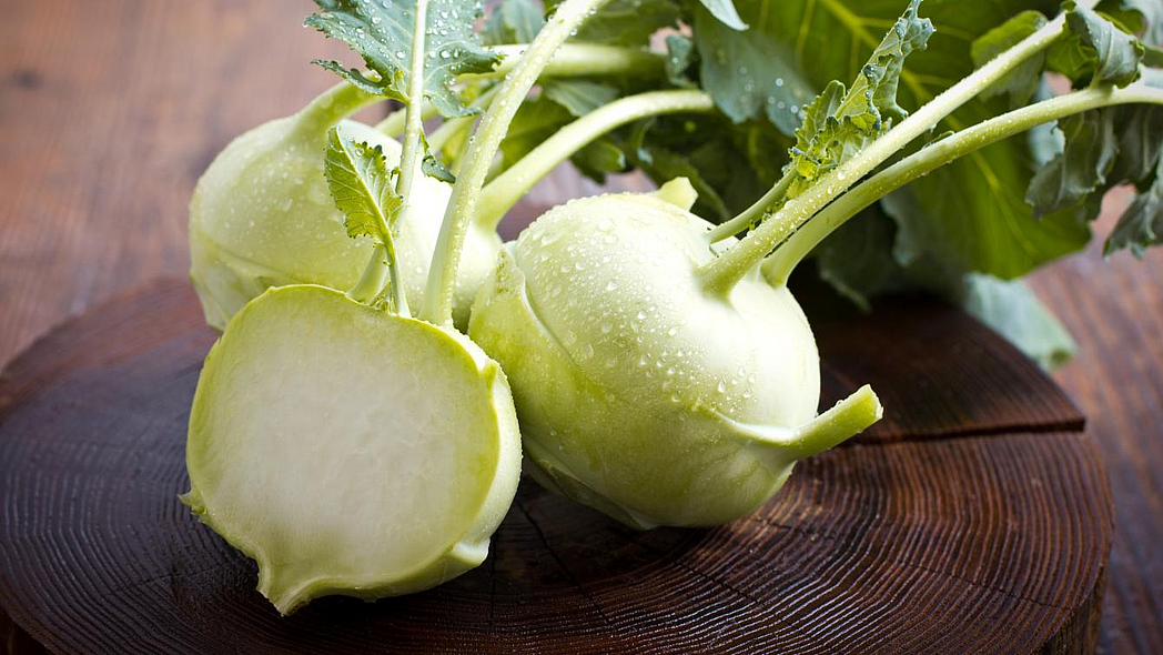 Zwei ganze und ein halber Kohlrabi mit Blättern auf einem runden Holzbrett