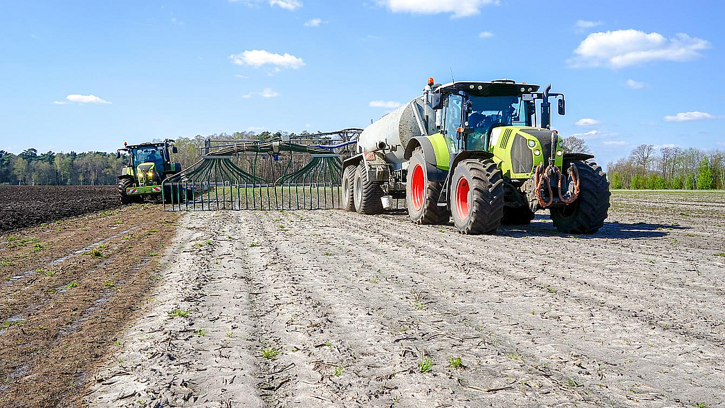 Traktor mit Güllefass und Schleppschlauchausbringung, links daneben ein Traktor mit Pflug, der die Gülle direkt einarbeitet.