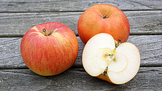 Zwei ganze und ein aufgeschnittener Apfel der alten Sorte Berlepsch auf einer Holzunterlage