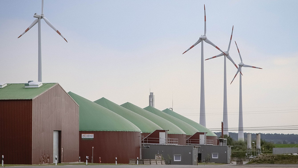 Biogasanlage mit Windrädern im Hintergrund