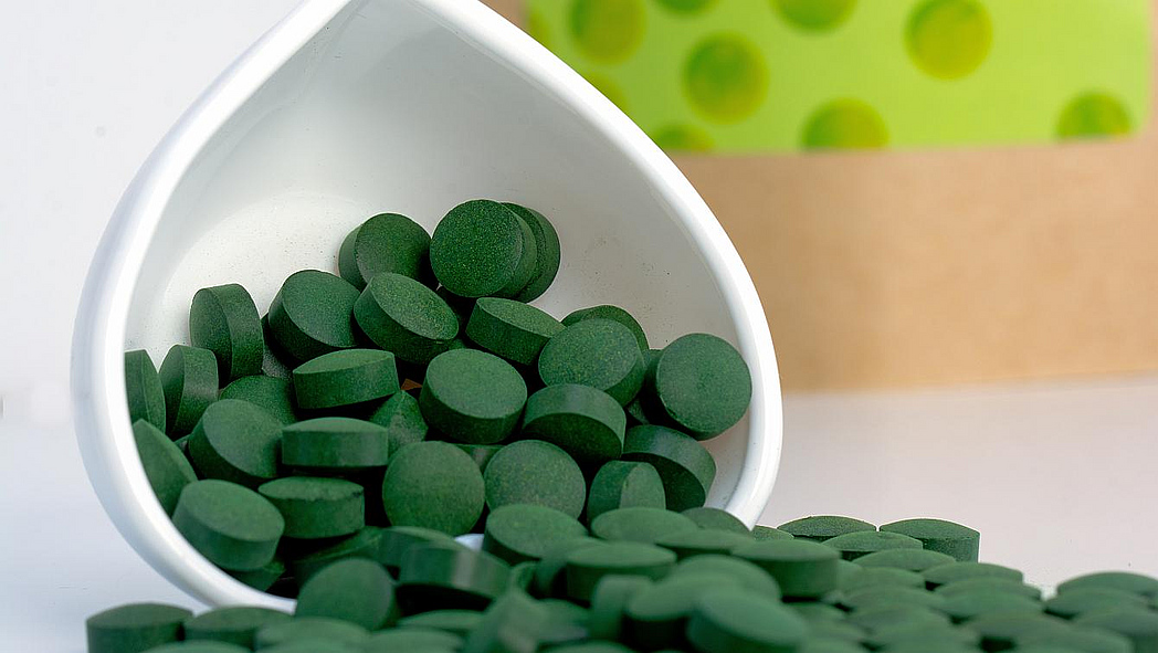 Grüne Tabletten liegen ausgekippt neben einer weißen Keramikschüssel.