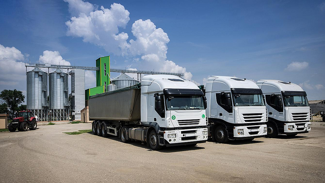 Drei große LKW parken nebeneinander vor einigen Getreidesilos