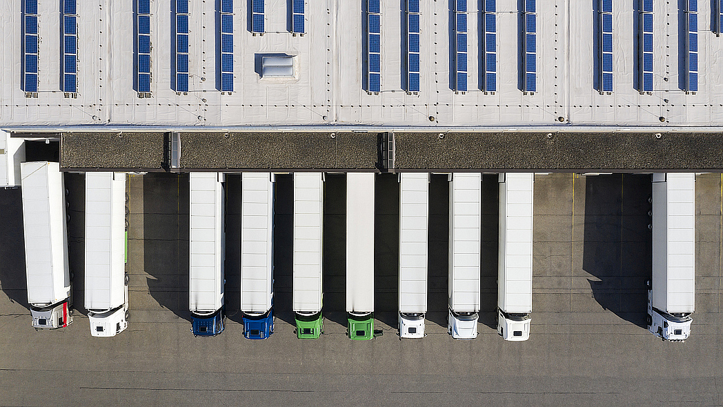 Aus der Vogelperspektive stehen mehrere LKWs parallel nebeneinander vor einer Lagerhalle.
