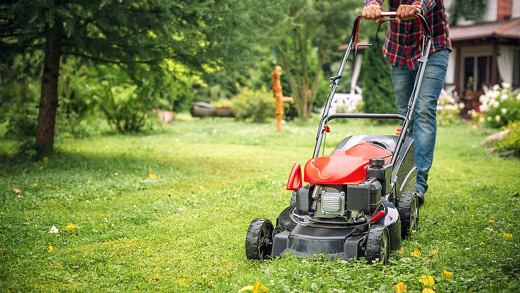 Mann mäht mit einem Rasenmäher den Rasen im Garten