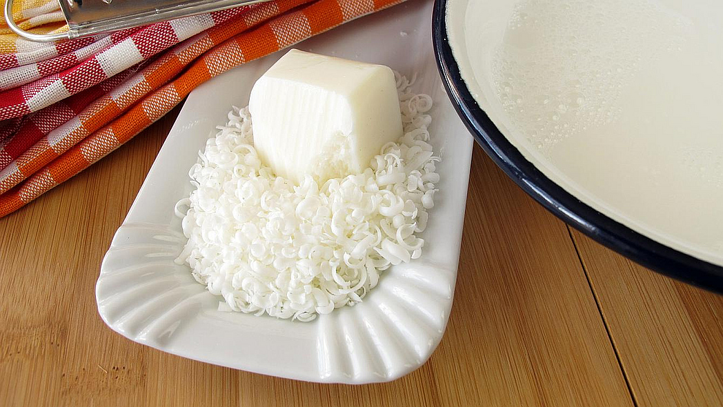 Ein Stück feste und geraspelte Kernseife mit Raspel und Schüssel mit Wasser auf einem Tisch.