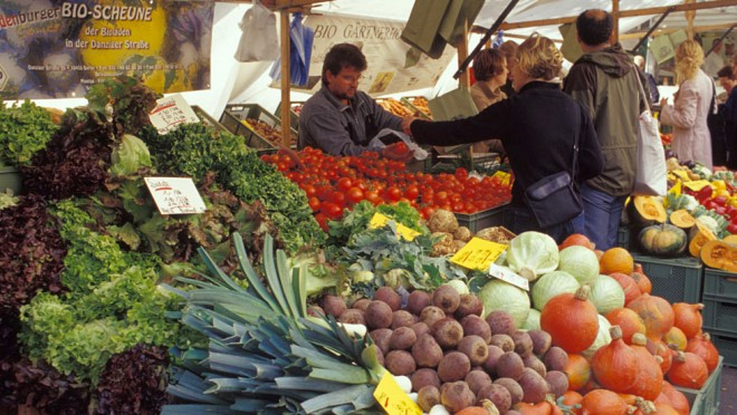 Einkaufssituation am Marktstand - ein Paar steht vor einen Gmüsestand und spricht mit dem Verkäufer.