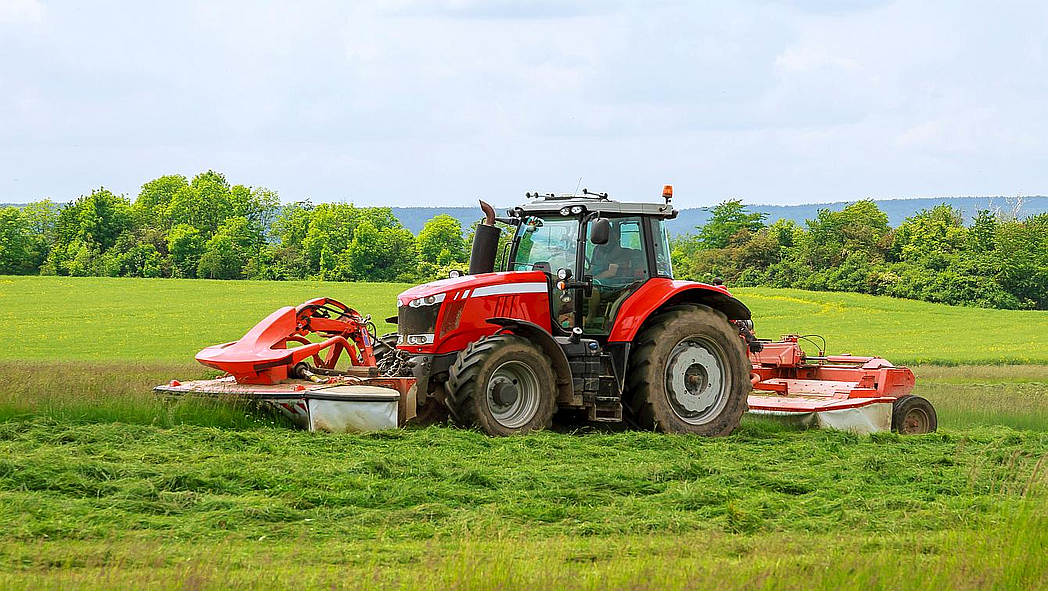Traktor mit Mähwerk im Einsatz auf einer Wiese.