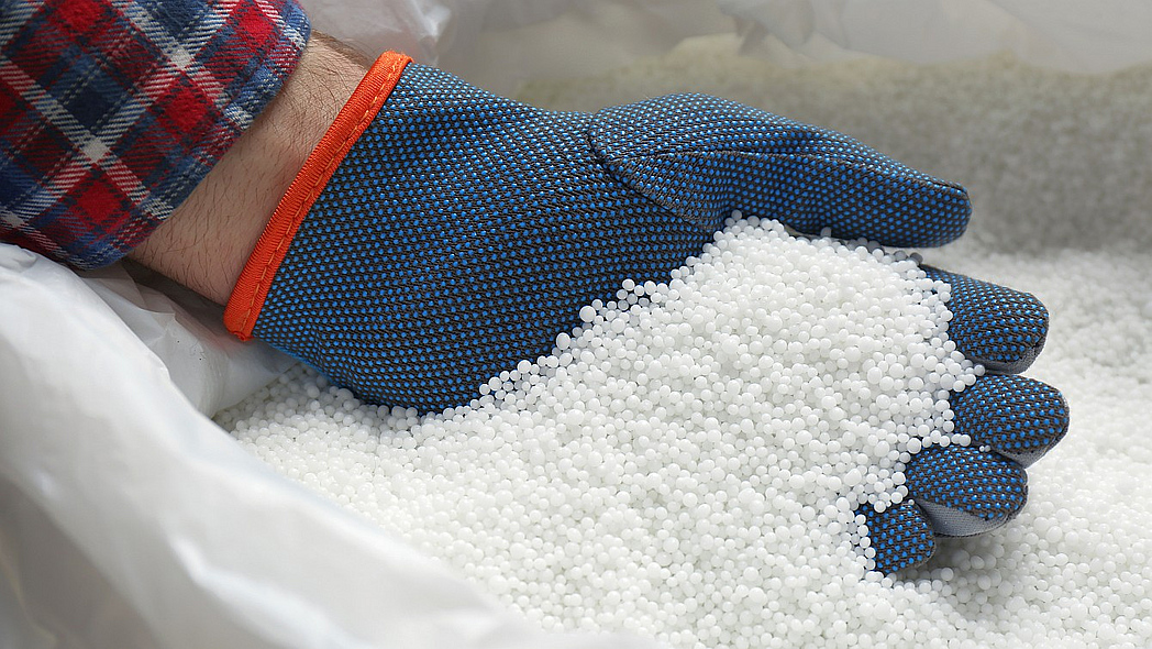 Behandschuhte Hand hält weißen Mineraldünger in körniger Form