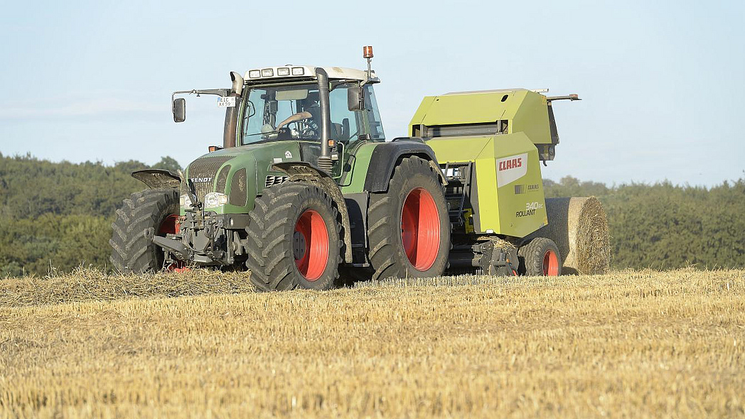 Traktor mit Rundballenpresse beim Strohpressen.