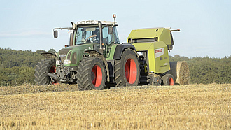 Traktor mit Rundballenpresse beim Strohpressen.