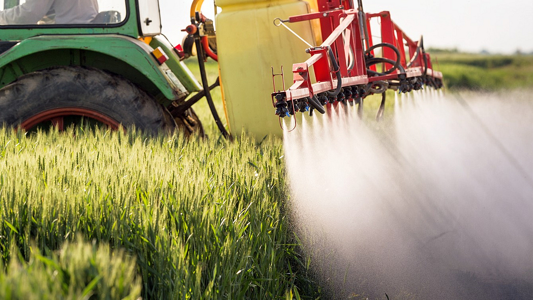 Traktor mit Pflanzenschutzspritze im Einsatz in einem Getreidefeld.