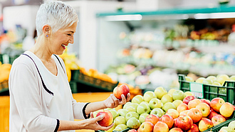 Eine Frau sucht im Supermarkt Äpfel aus.
