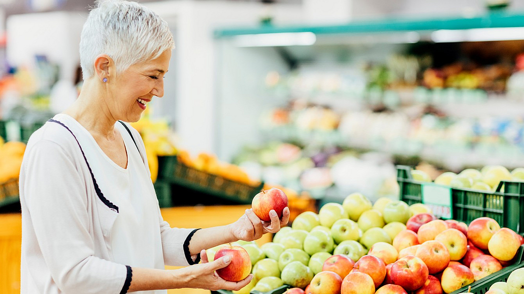 Eine Frau sucht im Supermarkt Äpfel aus.