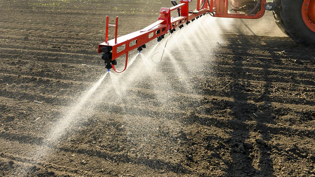 Pflanzenschutzmittel werden mittels einer Spritzdüse und einem Traktor auf ein Feld gesprüht