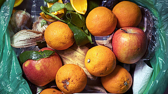 Orangen und Äpfel in einer Mülltonne