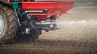 Ein Traktor mit Düngerstreuer bringt Dünger auf einem Feld aus