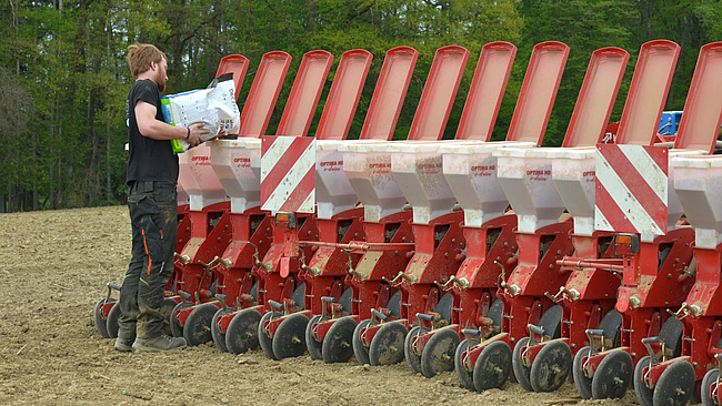 Landwirt befüllt die Säkästen eines 18-reihigen Einzelkornsägerätes mit Energiemaissaatgut