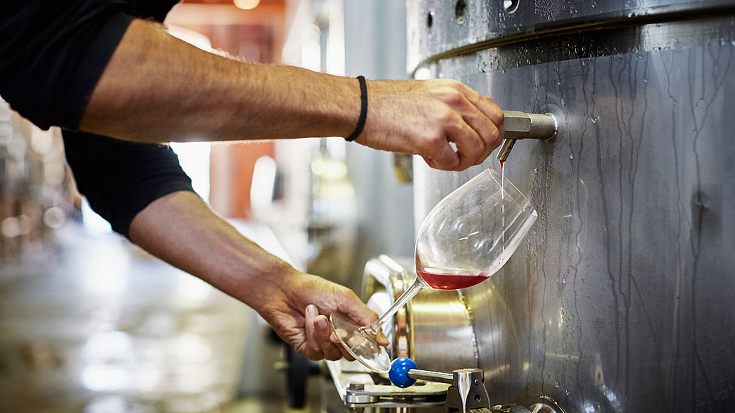 Mann füllt Rotwein aus einem Edelstahltank in ein Glas.