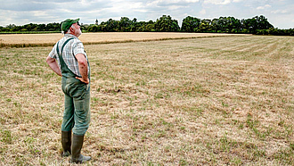 Landwirt steht auf einer vertrockneten Wiese und schaut in den Himmel