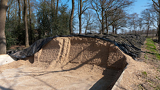 Fahrsilo mit Betonplatte, in dem Maissilage gelagert wird. Die Silage ist mit einer schwarze Folie und Reifen abgedeckt. An einer Seite ist das Silo geöffnet, um das Futter zu entnehmen.