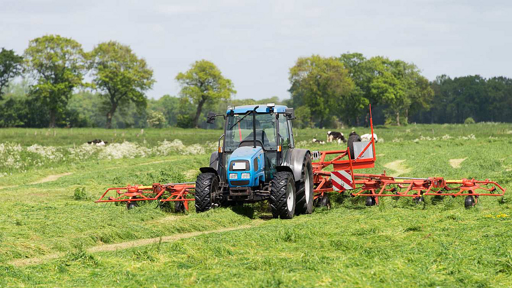 Traktor mit Zetter im Einsatz auf einer gemähten Wiese.