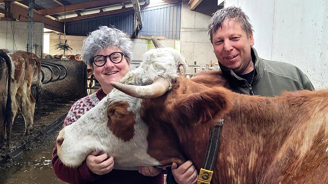 Eine Landwirtin und ein Landwirt stehen mit einer Kuh in einem Stall