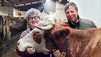 Eine Landwirtin und ein Landwirt stehen mit einer Kuh in einem Stall